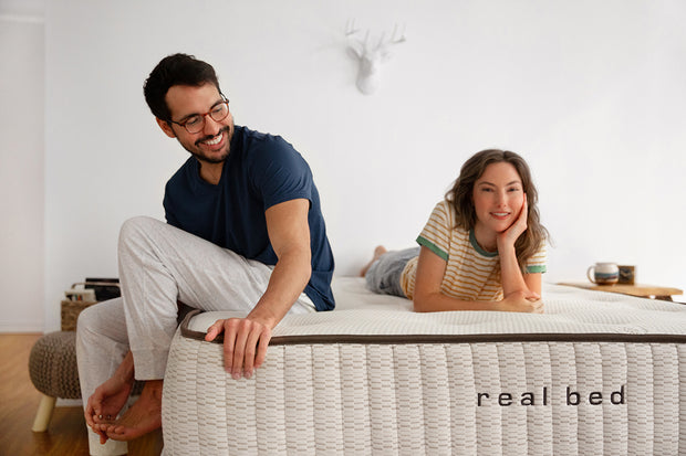 Man sitting and woman laying on a Real Bed natural mattress. Image. 